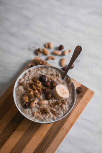 Bowl of healthy oatmeal topped with banana slices, walnuts, hazelnuts, and peanuts.