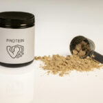 Protein powder for fat loss: A tub of protein powder with a flexing arm icon, alongside a scoop filled with brown powder on a white surface, representing a key supplement for weight management.