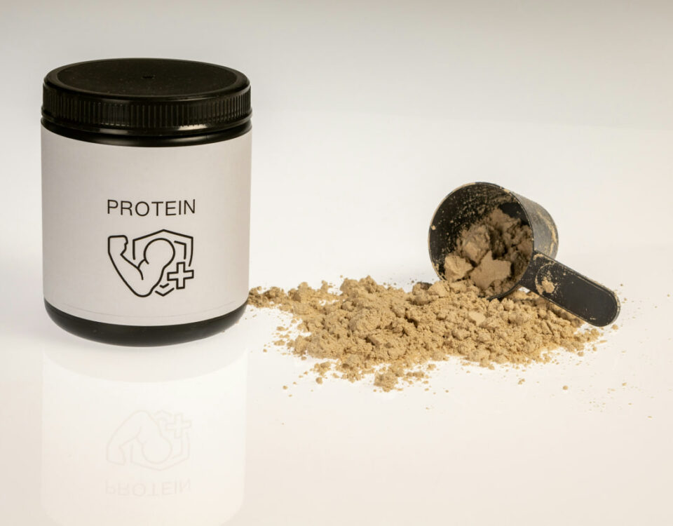 Protein powder for fat loss: A tub of protein powder with a flexing arm icon, alongside a scoop filled with brown powder on a white surface, representing a key supplement for weight management.