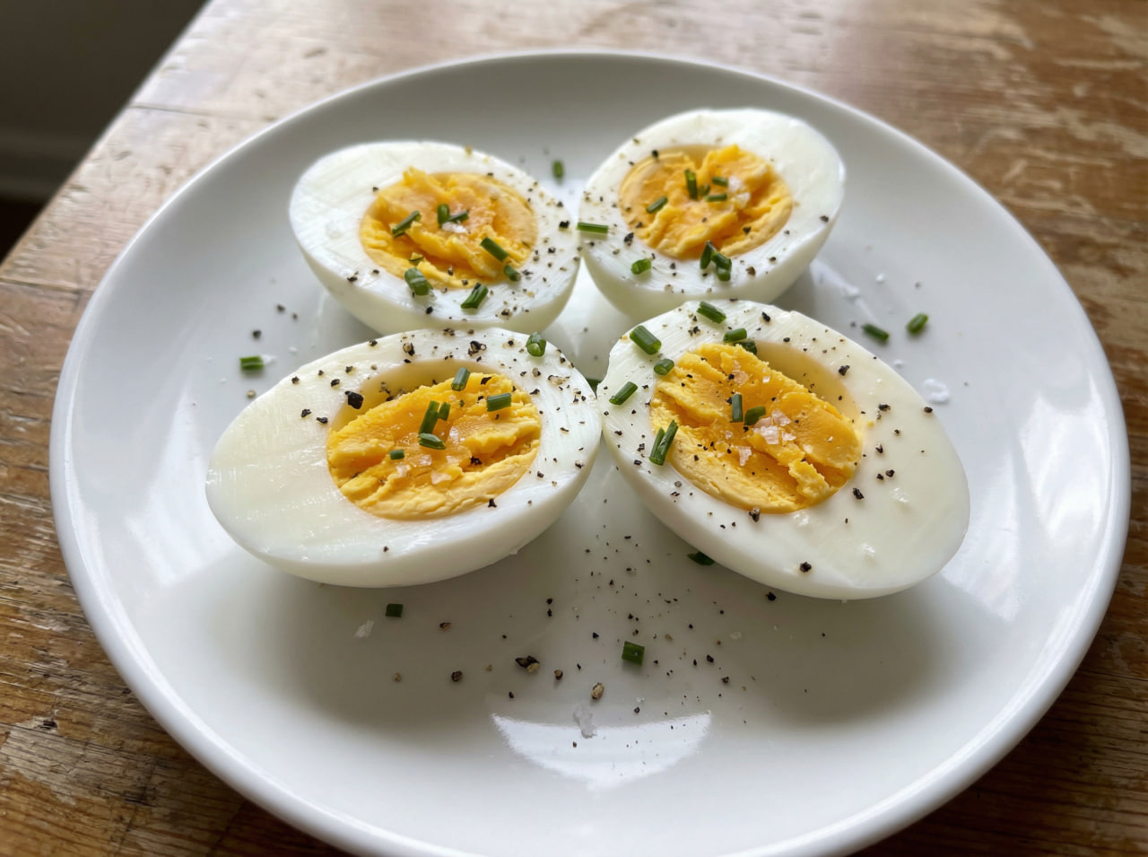 Halved hard-boiled eggs seasoned with black pepper, sea salt, and fresh chives on a white plate – a simple, budget-friendly high-protein snack